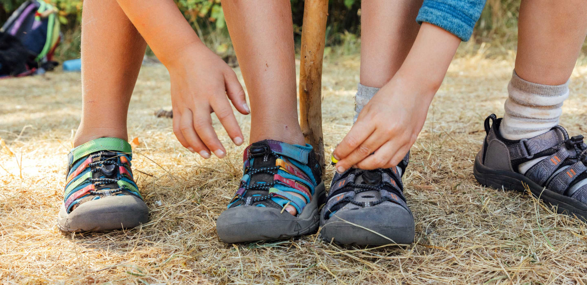 Kids wearing KEEN closed toe sandals outside and reaching down to tighten their shoes