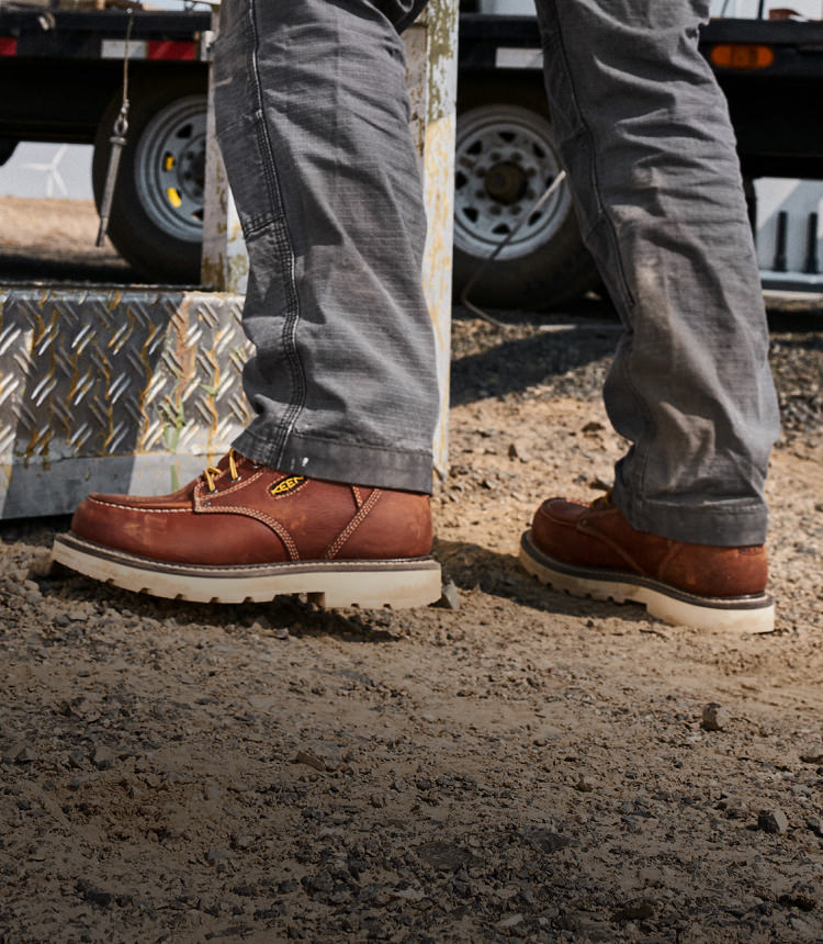 Waist down shot of man wearing Cincinnati work boots and jeans standing on dirt surface